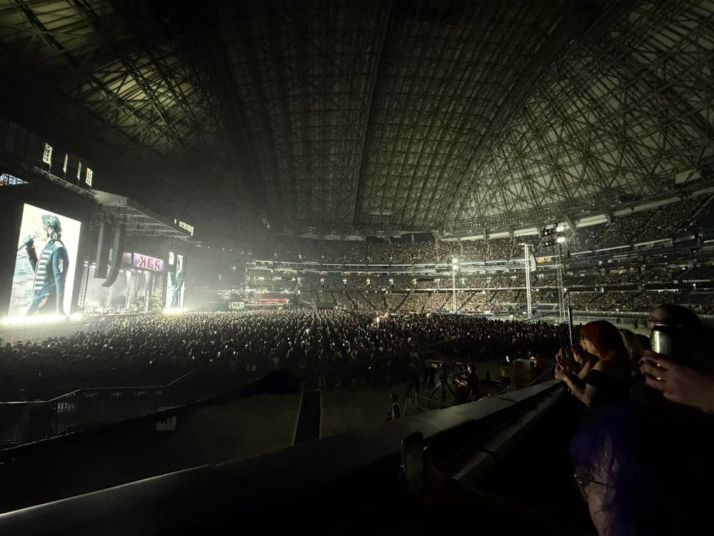 Wide angle photo of a stadium showing crowd on the right, stage on the left, and stadium dome at the top.