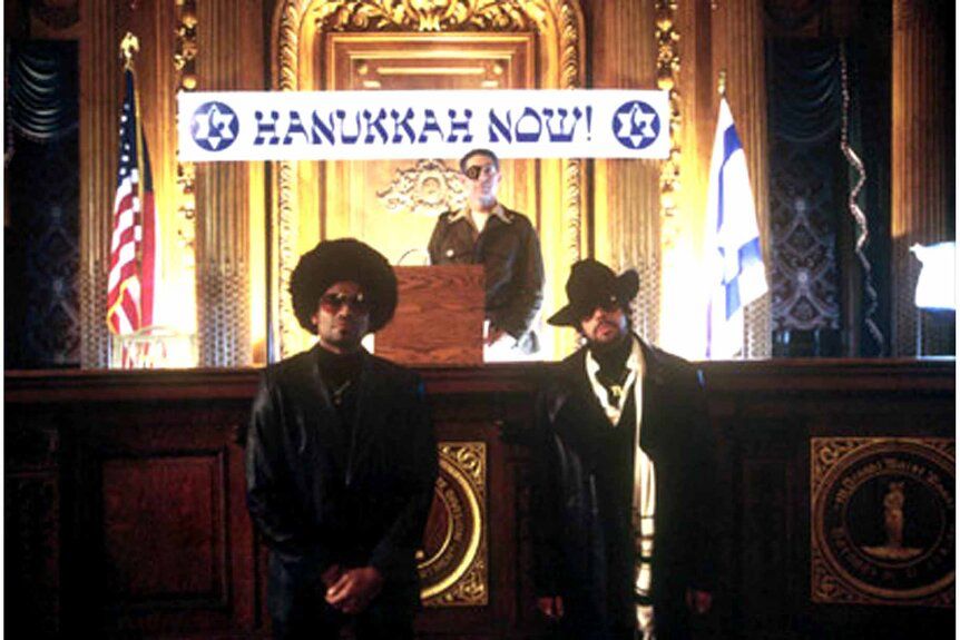 Some tough-looking guys who are probably Jewish standing in front of a banner that reads “HANUKKAH NOW!” from The Hebrew Hammer