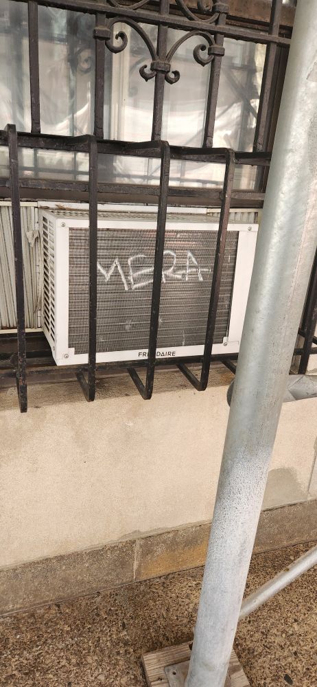 Window air conditioning unit in a ground floor apartment with the word MERA carved into it.