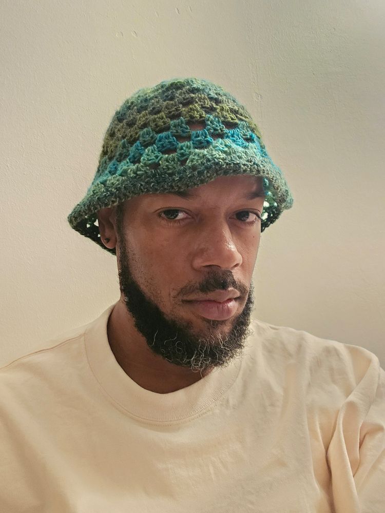 Black man wearing green crochet bucket hat, facing right