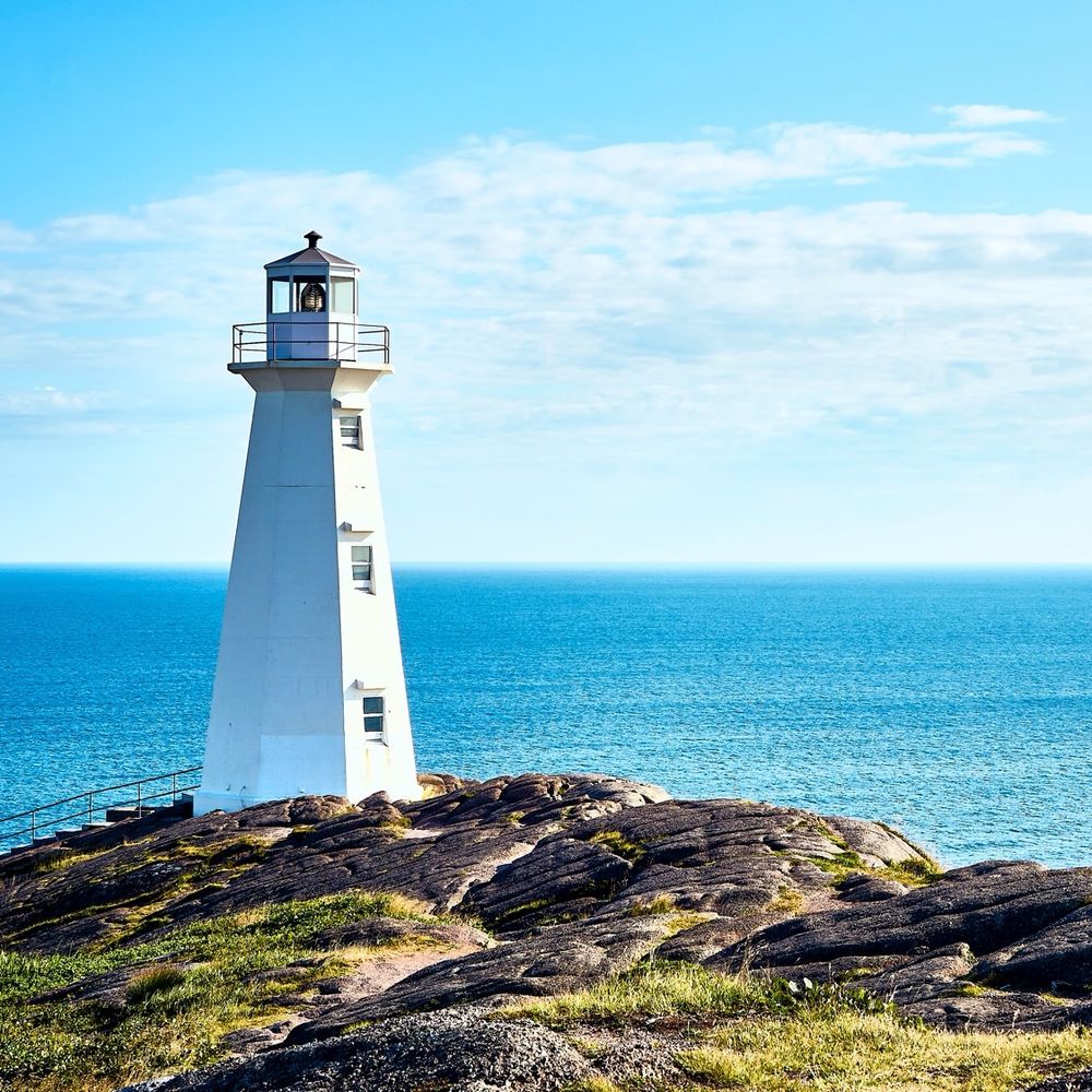 Lighthouse on a hill with blue ocean and sky in background 