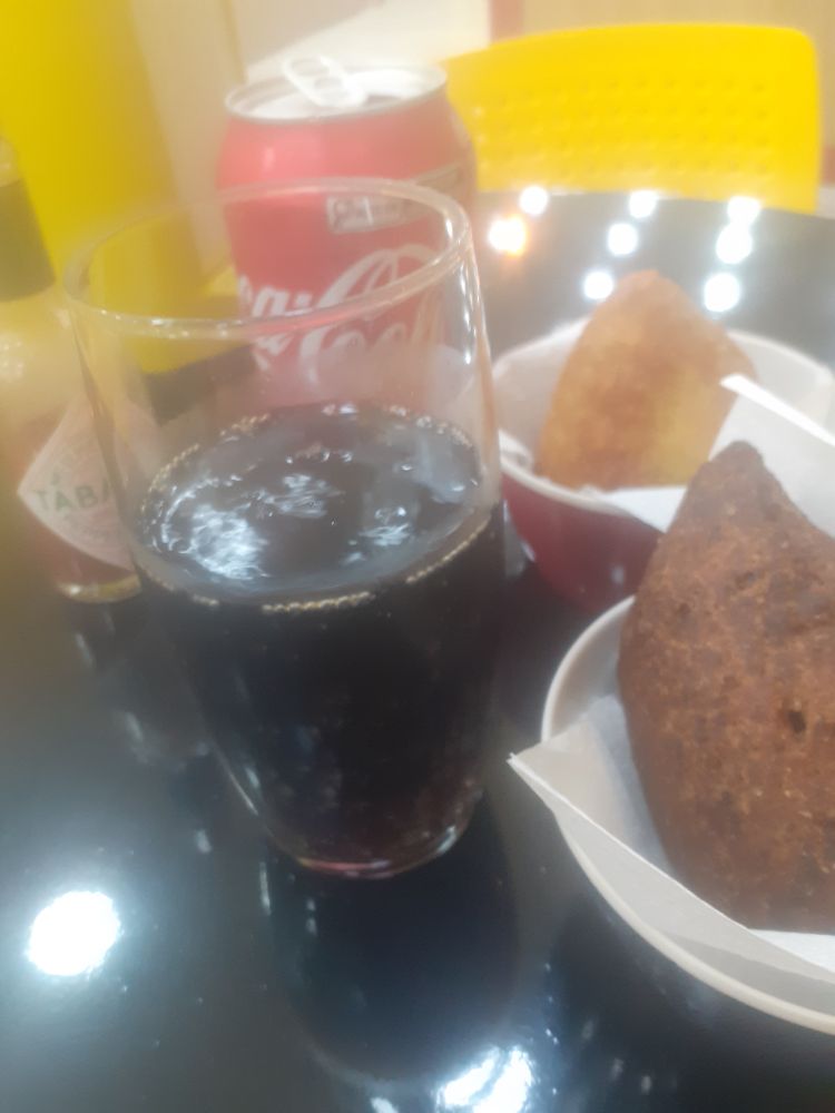 Copo de Coca cheio, latinha atrás, molhinho de pimenta, uma coxinha e um quibe ao lado.