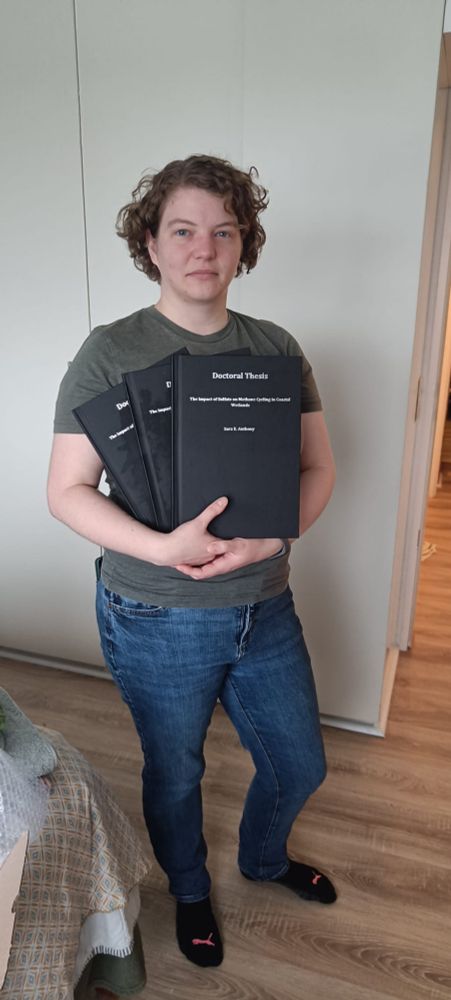 I am standing with three black hardbound doctoral thesis books in my arms, with a generally neutral look on my face because apparently I couldn't smile normally.