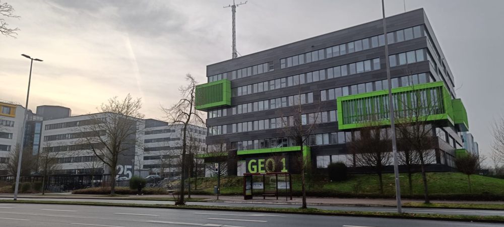 A view of the GEO1 building at the University of Münster, which houses the Institute of Landscape Ecology (ILÖK) and my new place of work. The building is grey with green bump out window accents around the lecture rooms, and has 6 floors plus a basement. Grey skies and other University buildings are visible in the background