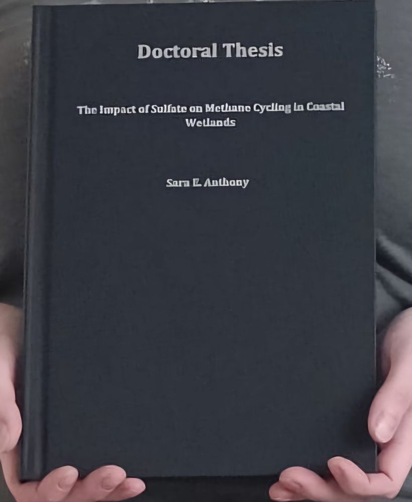 A zoomed in view of the cover of one copy of my black hardcover bound thesis, with three lines of text in silver:

"Doctoral Thesis"

"The Impact of Sulfate on Methane Cycling in Coastal Wetlands"

"Sara E. Anthony"