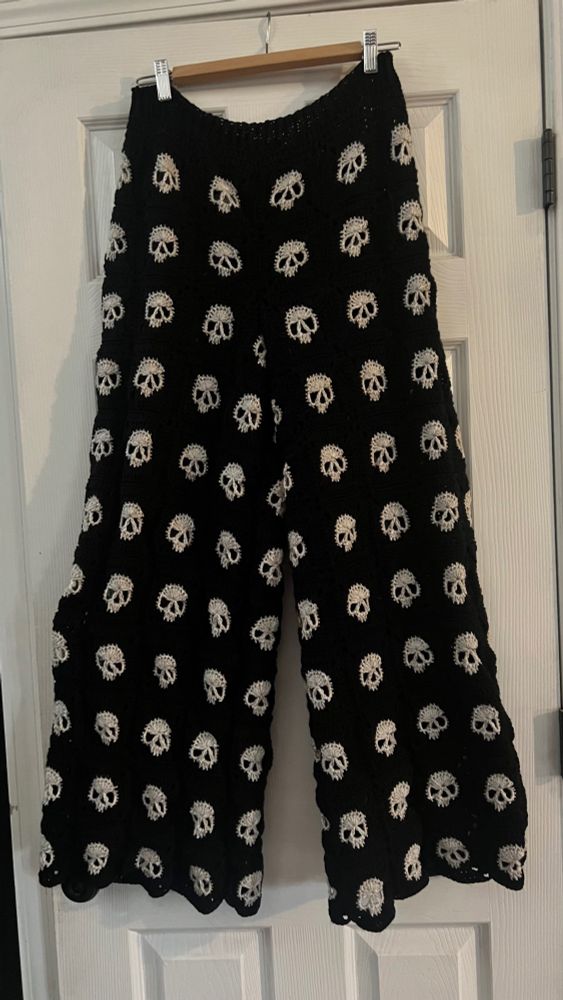 Picture of crocheted pants that are made from black granny squares with ivory skulls on them. 