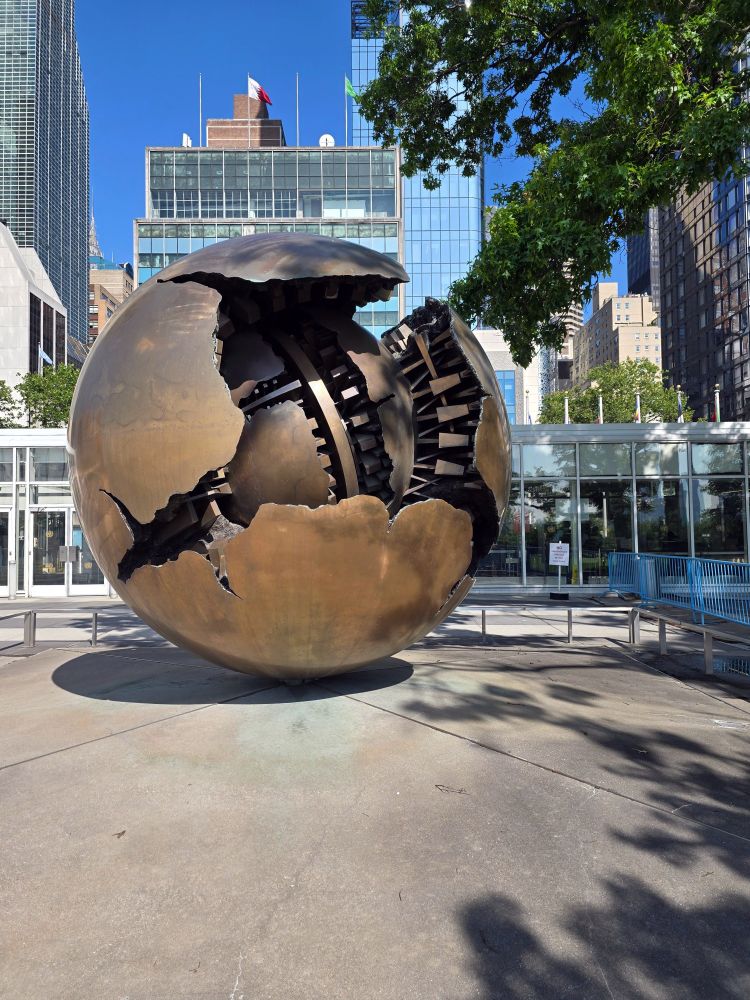 Vor dem Hauptgebäude der Vereinten Nationen in New York steht die Bronze-Skulptur „Sphere within Sphere“ von Arnaldo Pomodoro. Das UN-Gebäude ist hinter der Skulptur zu erkennen.