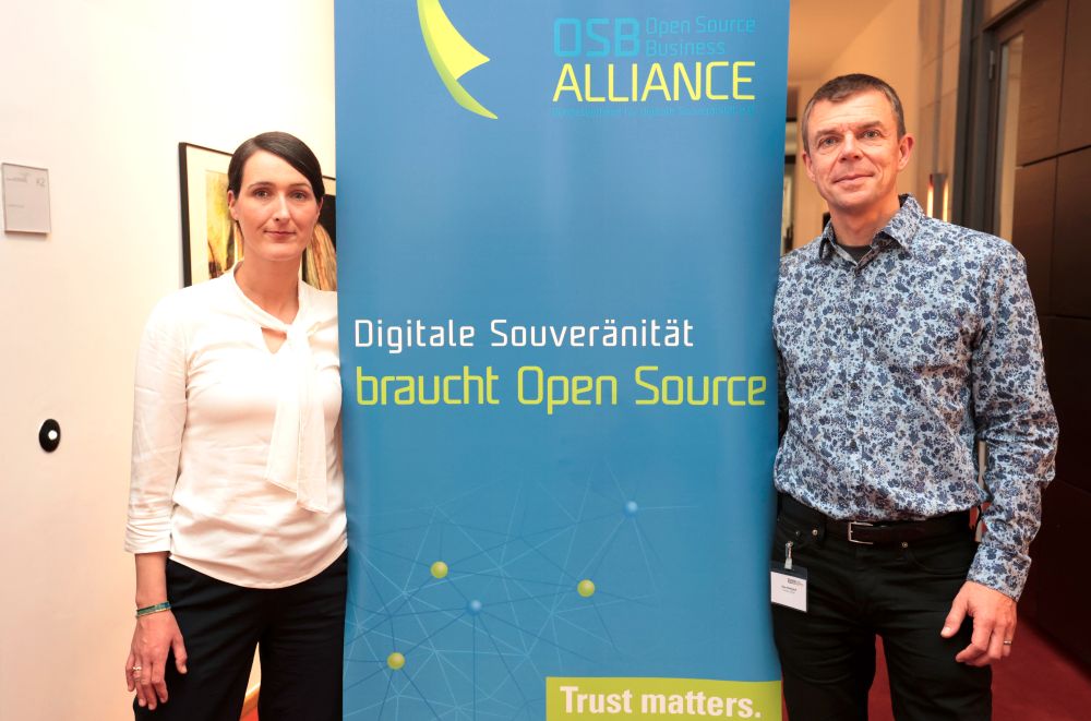 Miriam Seyffarth und Claus Wickinghoff stehen rechts und links neben einem Rollup der Open Source Business Alliance, auf dem &quot;Digitale Souveränität brauch Open Source&quot; und &quot;Trust matters&quot; steht, beide Personen schauen freundlich in die Kamera.
