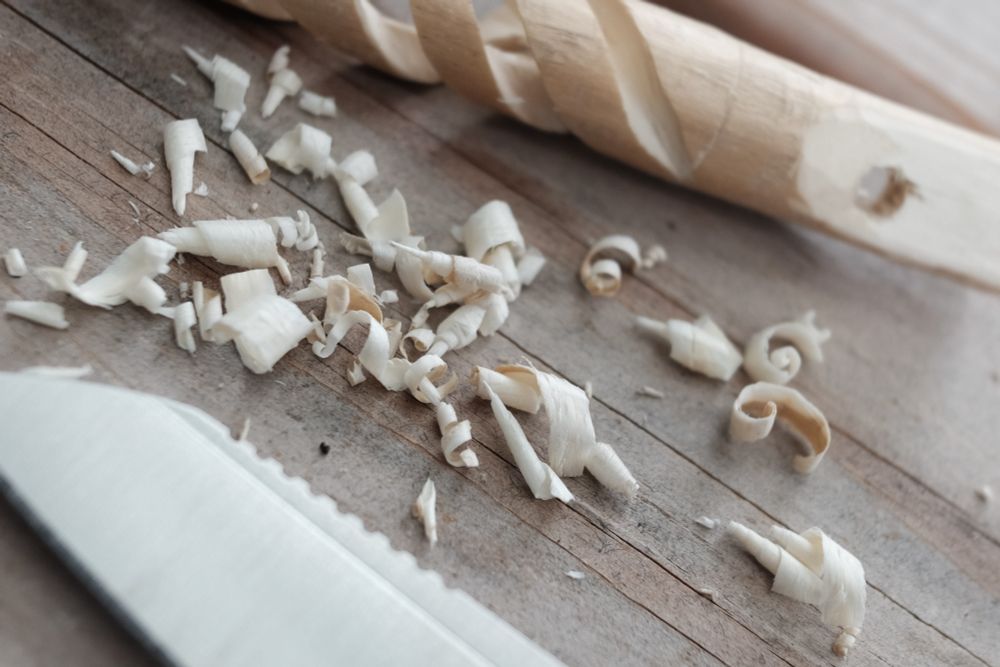 Many wood shavings next to a whittled spiral and a knife blade. 