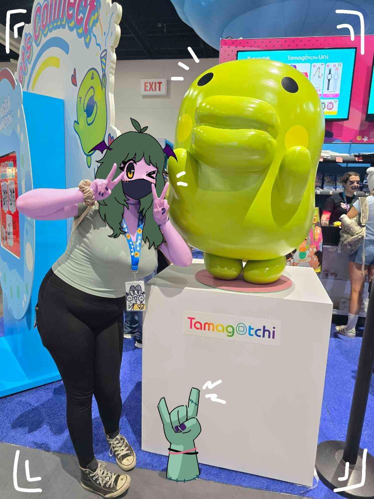 edited picture of miel posing next to a statue of Kuchipatchi from Tamagotchi, she has both her arms up in peace signs and her face is drawn in to look like her vtuber character 