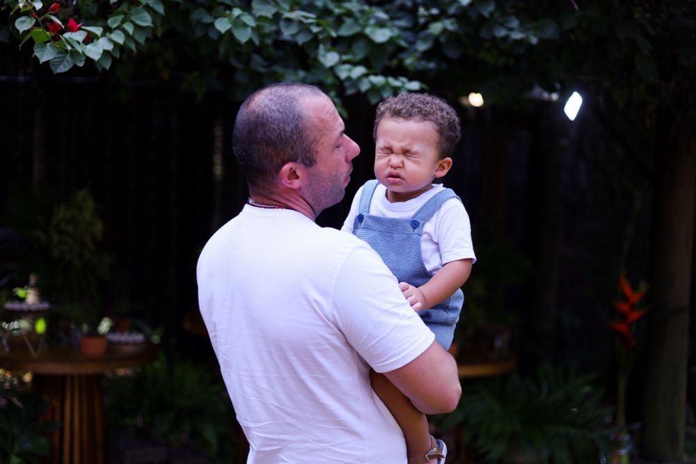 Um bebê fofo de uns 3 anos espirrando no colo do pai 