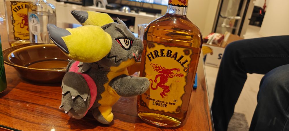 Bean, a Deformed Nergigante plushie, climbing a bottle of Fireball 