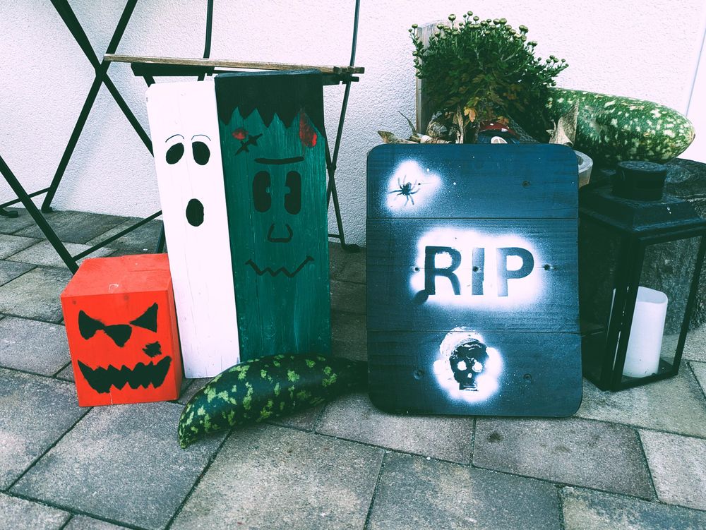 Some Halloween decorations in front of our house. A big black board with a spider and a skull saying "RIP". A mean pumpkin, a zombie and a ghost.