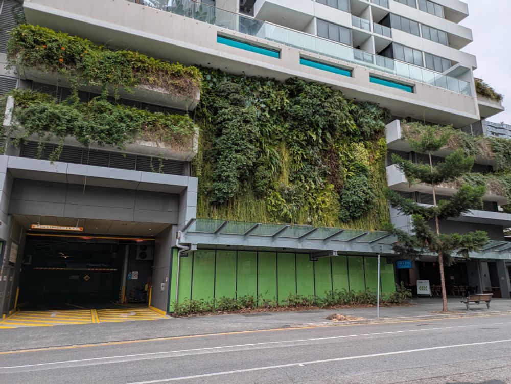 A photo of a green building facade in Brisbane. One section hosts a solid wall of plants, while the adjacent sections have plants spilling out over balconies.