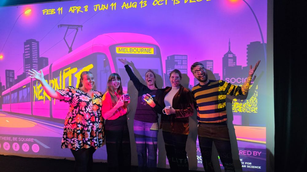 A photo of the two Nerd Nite bosses, Dr Ebony Monson and Dr Wade Kelly, with the three speakers from the evening: Dr Kira Hughes, Dr Jacinta Humphrey and Dr Veronique Paris. Behind them is a Nerd Nite artwork image of a bright pink tram.