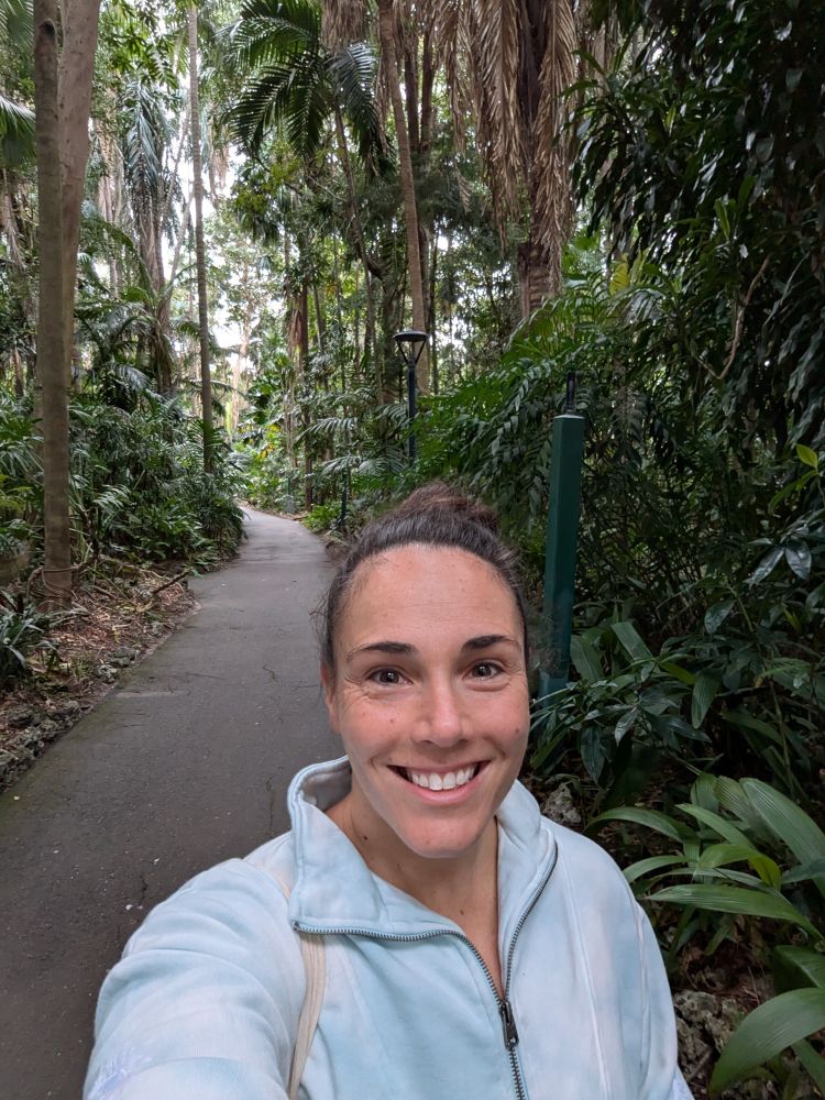A selfie of Dr Jacinta Humphrey in the Brisbane City Botanic Gardens. She is smiling at the camera and is surrounded by lush, green palms.