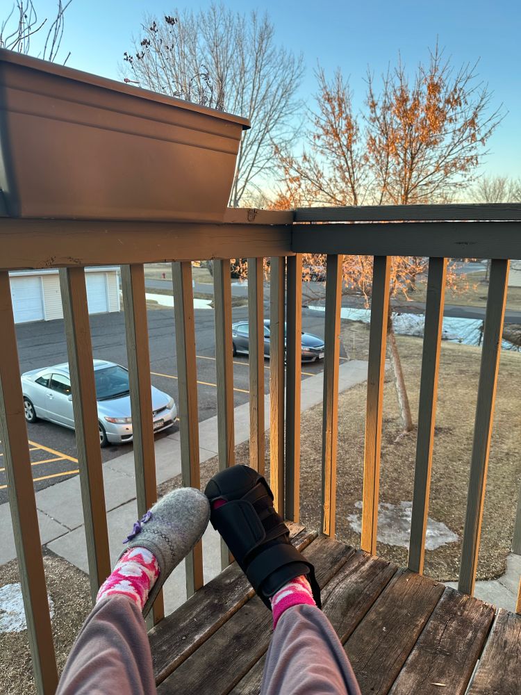 Two feet posed on a porch, one wearing a medical boot to help heal and stabilize.