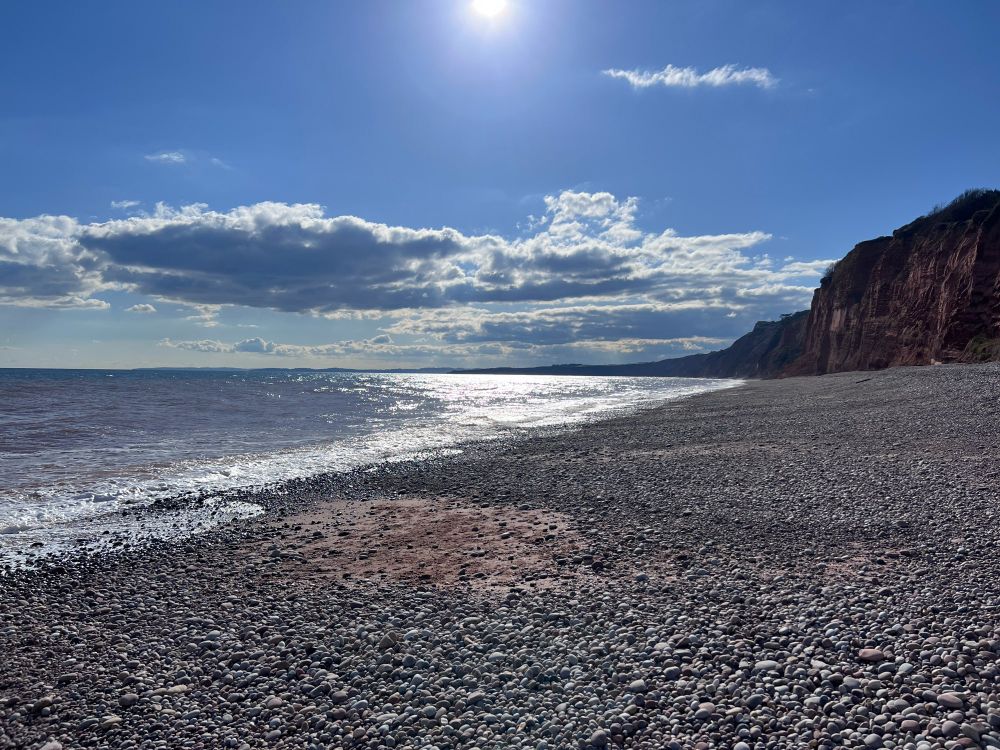 Sun reflecting off sea next to red cliffs and stony beach at Budleigh 