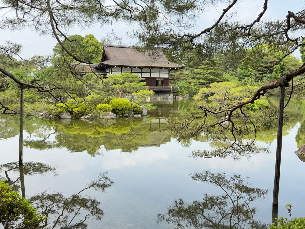 Kleiner japanischer Tempel von Büschen und Bäumen umgeben, der sich in einem Teich widerspiegelt.