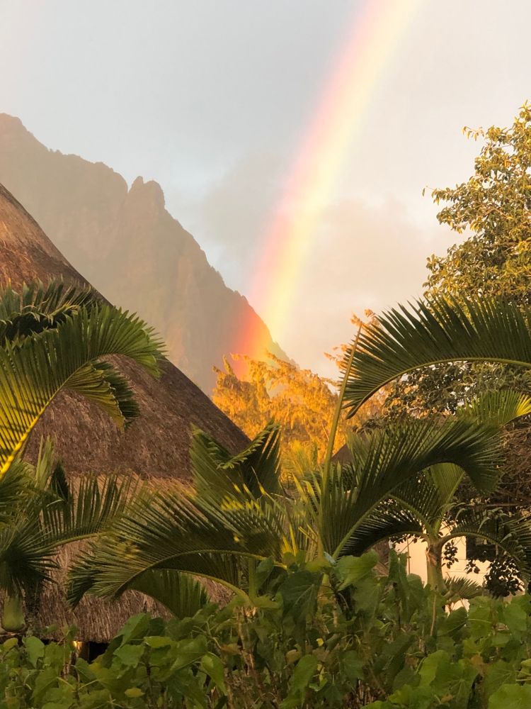 Teil eines Regenbogens, endet in tropischer Landschaft zwischen zwei Hügeln