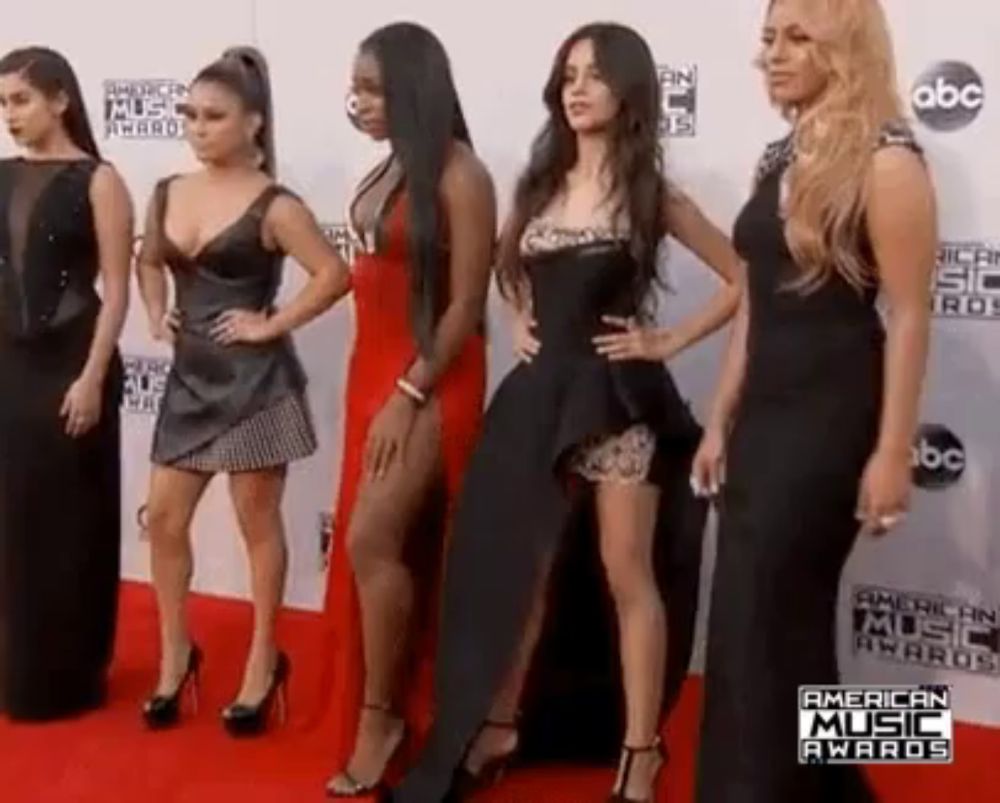 a group of women are standing next to each other on a red carpet at an american music awards .