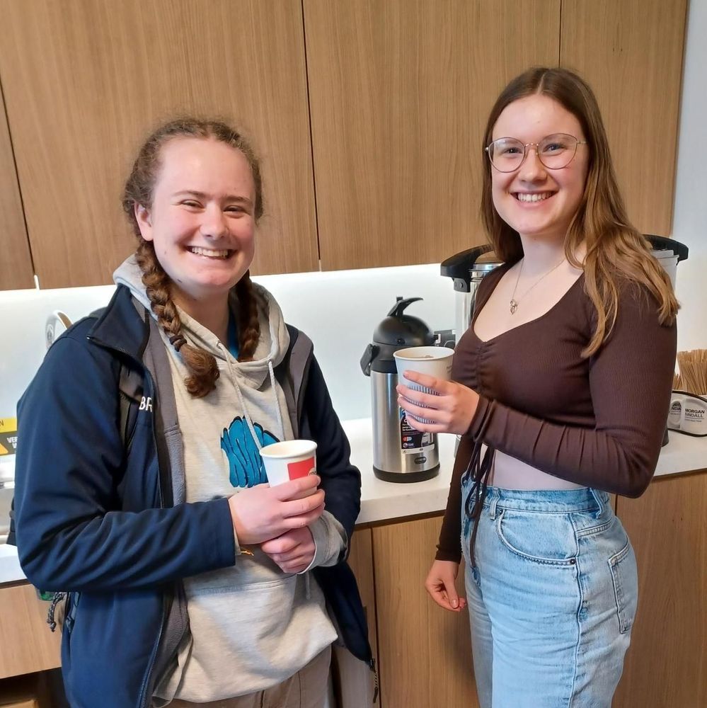 Photograph of two young women smiling and holding paper cups.
