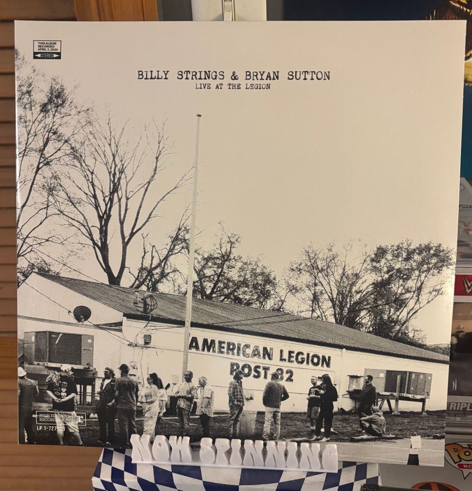 The cover of Billy Strings & Bryan Sutton's album Live at the Legion displayed on a stand that says "now spinning".