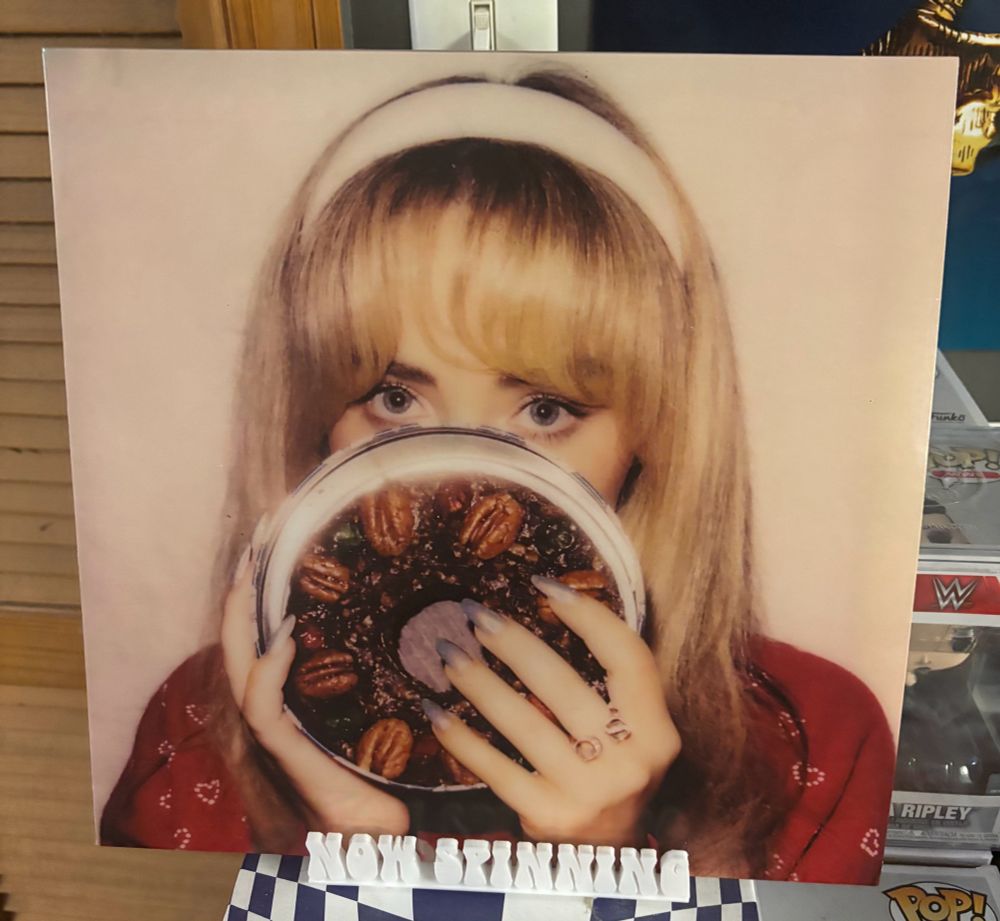 The vinyl cover of Sabrina Carpenter's fruitcake EP, displayed on a stand that says "now spinning".