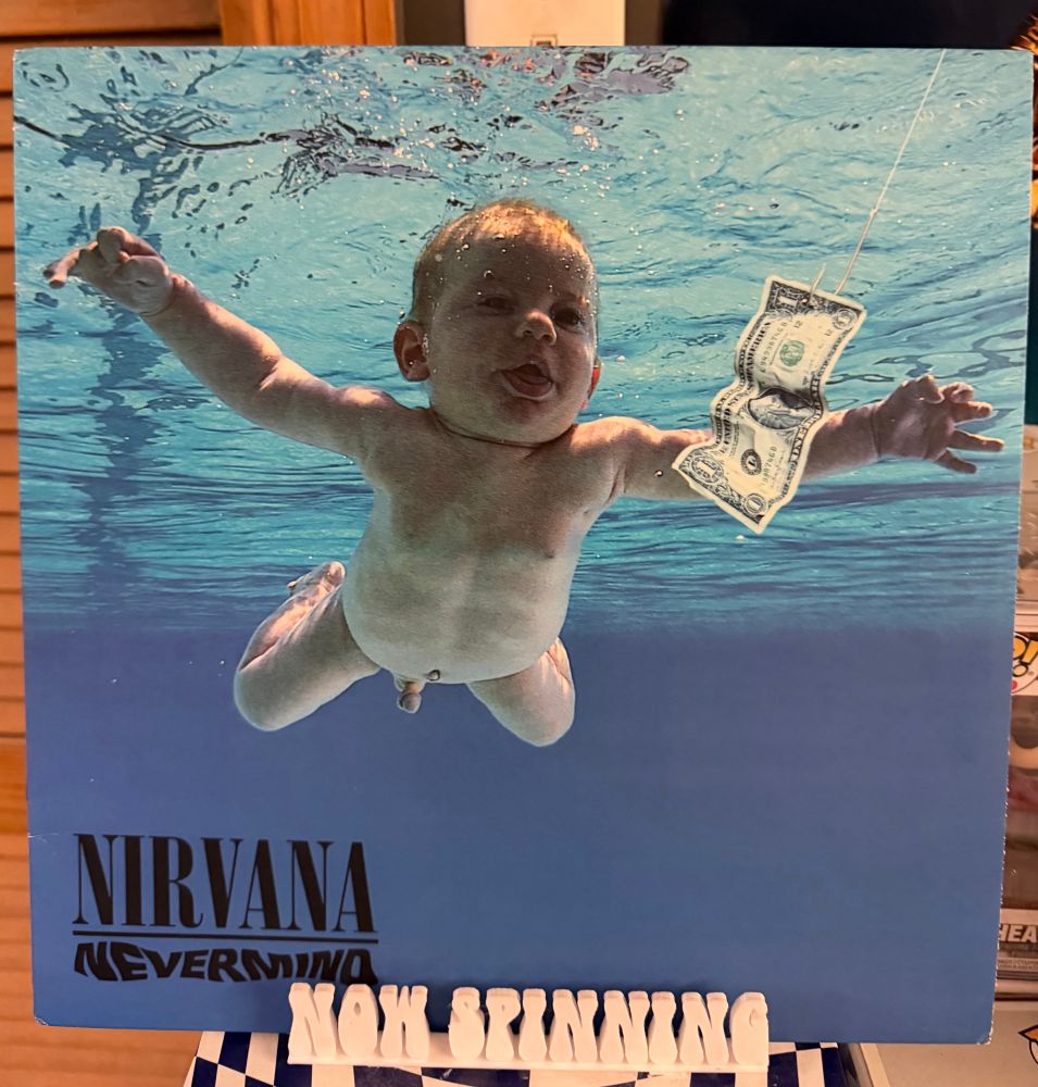 The cover of Nirvana’s album Nevermind displayed on a stand that says “now spinning”.