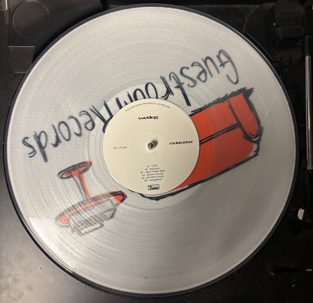 The vinyl of Wet Leg's album moisturizer sitting on a turntable. The vinyl itself is clear.