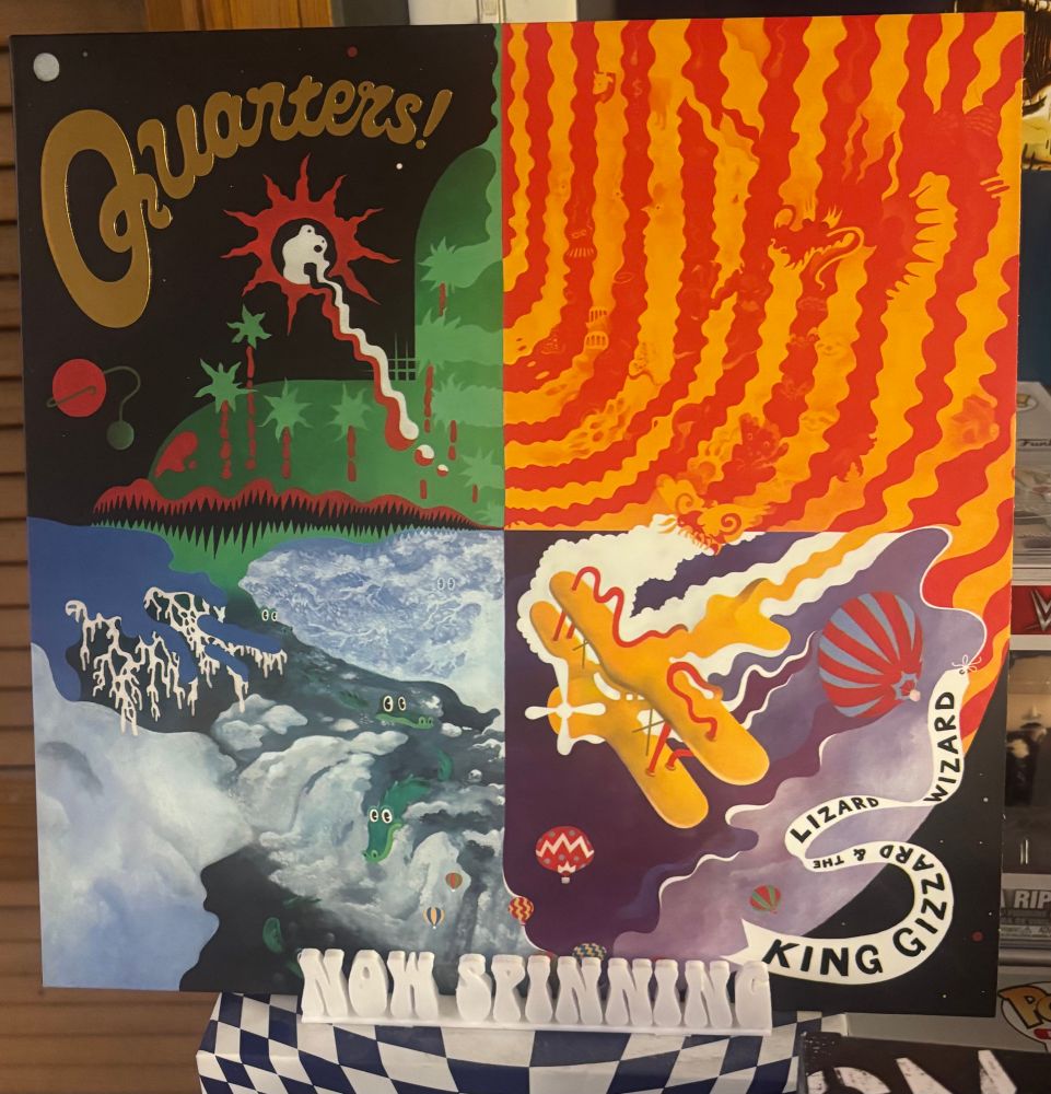 The cover of King Gizzard & The Lizard Wizard's album Quarters! displayed on a stand that says "now spinning".