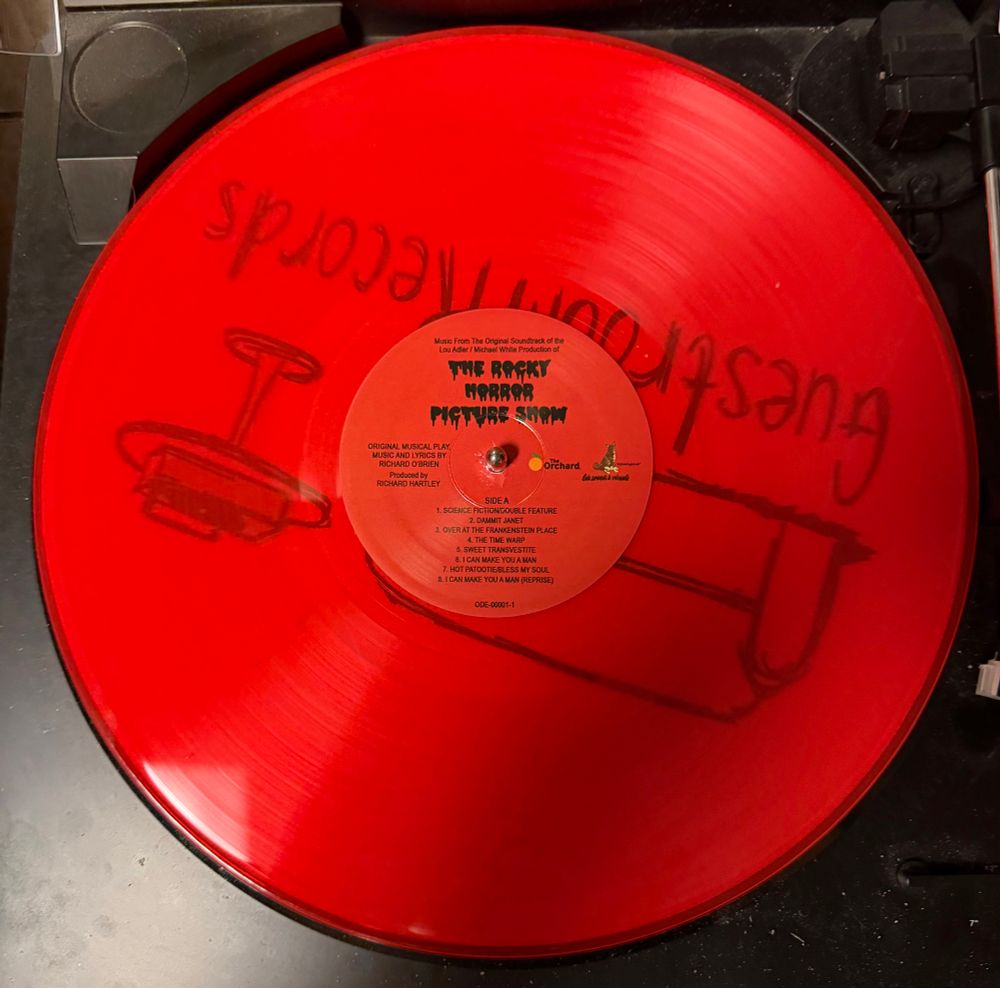 The vinyl of the soundtrack for the film The Rocky Horror Picture Show sitting on a turntable. The vinyl itself is a translucent red color.