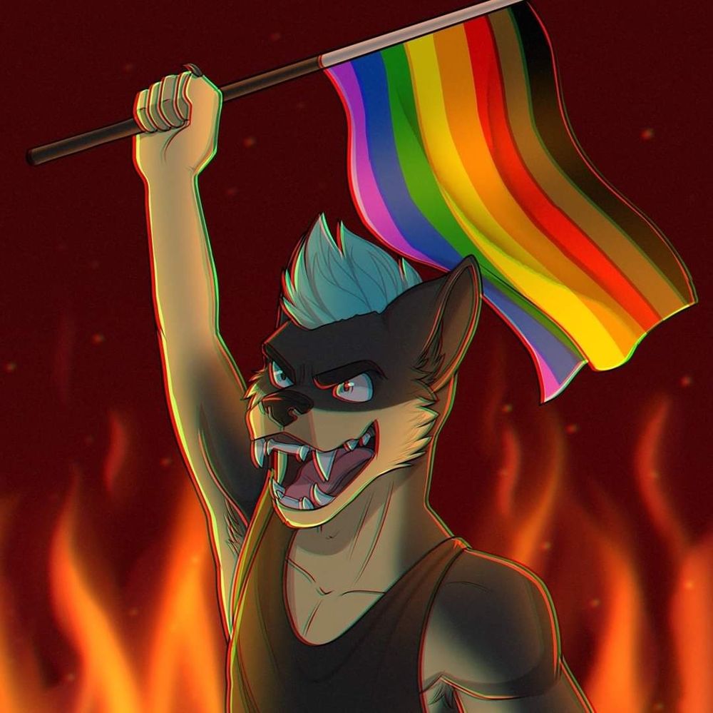 Taxtm in a black tank-top, with an inclusive flag raised high. Flames are in the background.