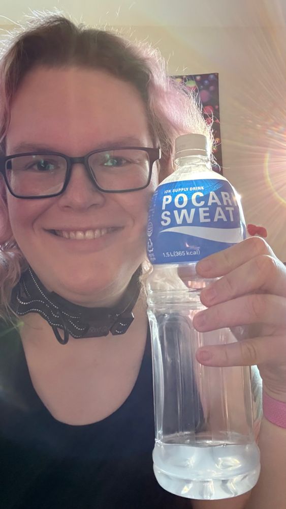 A picture of Delta holding up a bottle of Pocari Sweat, while smiling at the camera.