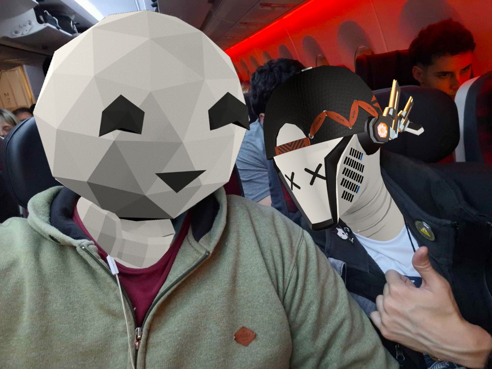 Photo of an airplane interior, with two people posing for the photo in the middle of the image. the one on the left with a round polygonal head smiling and the one on the right with a robot head with a neutral expression wearing a cap and headphones.