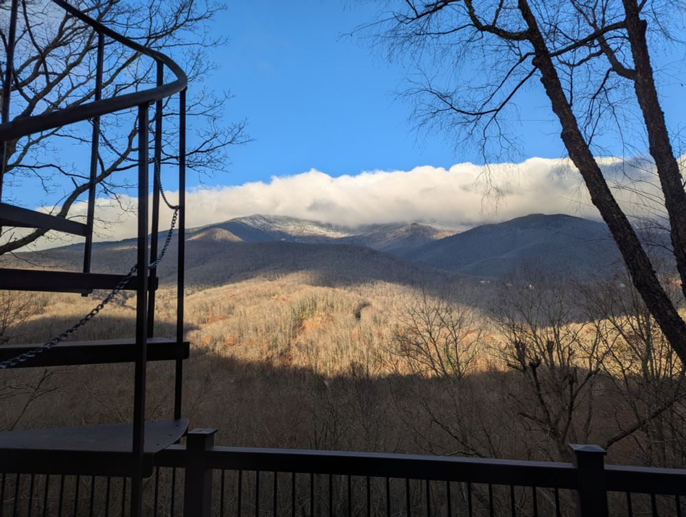Mt Mitchell NC morning bright blue sky, with very thick cap of clouds, snow on the ground at the evergreen line 