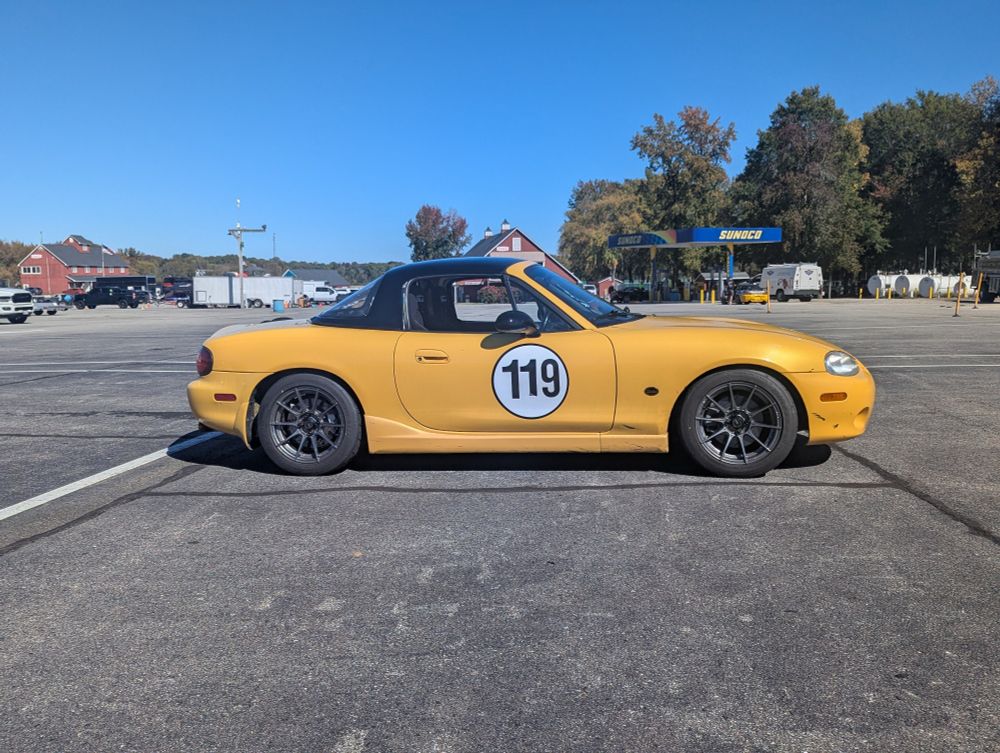 My car with my old set of wheels. Bright yellow Miata alone in a parking lot 