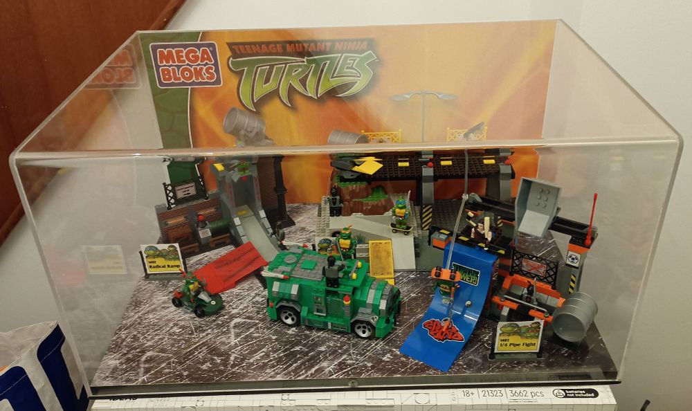 A plexiglass box containing several Mega Bloks Teenage Mutant Ninja Turtle Sets: 1402 Radical Ramp, 1401 1/4 Pipe Fight, 1411 Battle Shell Bridge.