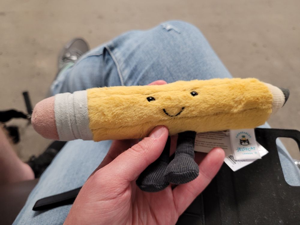 A Jellycat plush toy of a pencil with an adorable smile and two little feet.