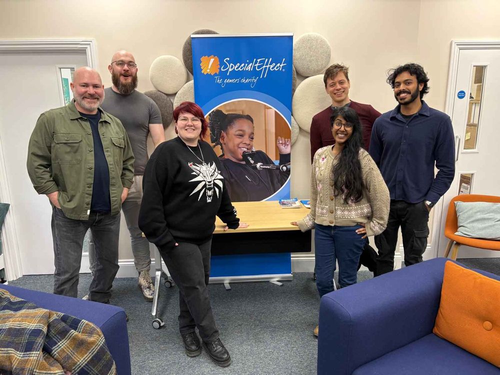 A group of people stand around a sign that says SpecialEffect. All are smiling broadly and look excited.