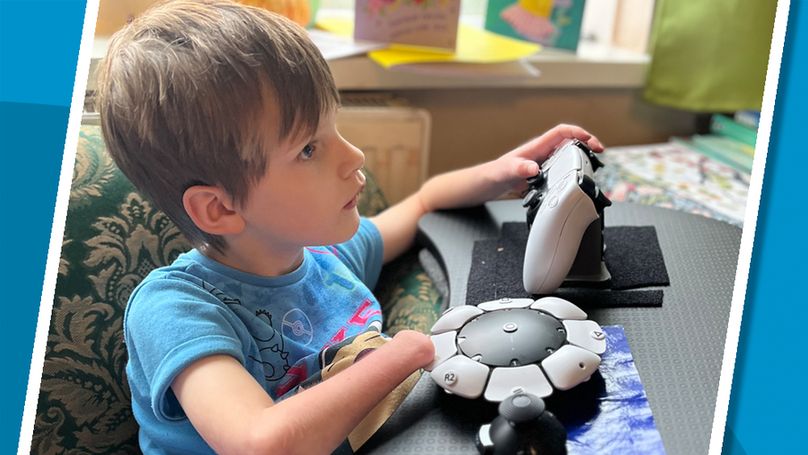 A young girl without a right hand wearing a snorlax shirt looks intently to the right, using a white accessible gaming control setup.