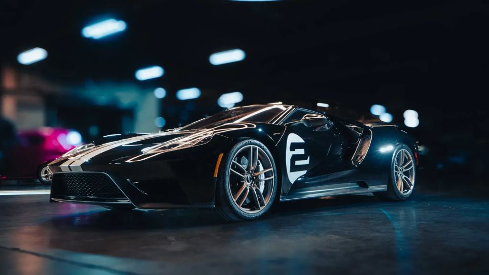 A black Ford GT with a white painted number two on the side in a dimly lit and blurred garage.