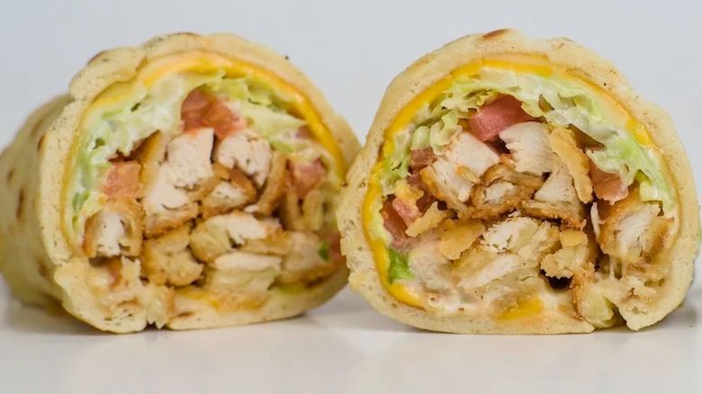 A Detroit Coney Island Hani wrap cut in twain: breaded chicken pieces, chopped letuce and tomato, a thin layer of melted yellow cheese, all wrapped inside a gyro-style flatbread. 