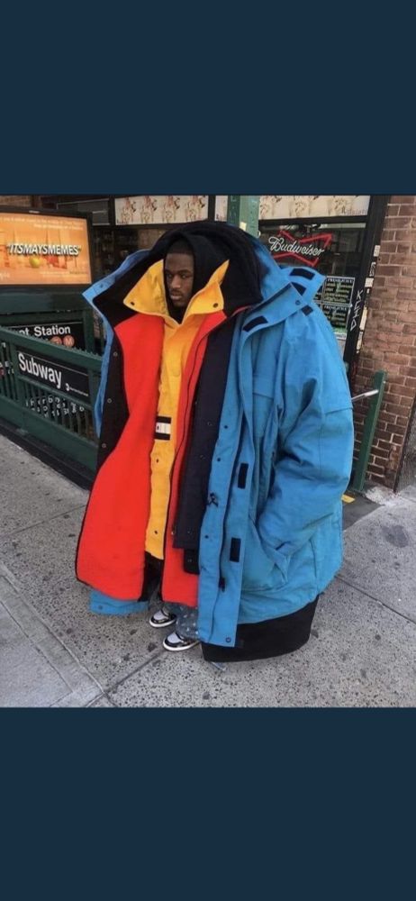 A black man wearing several very large coats 