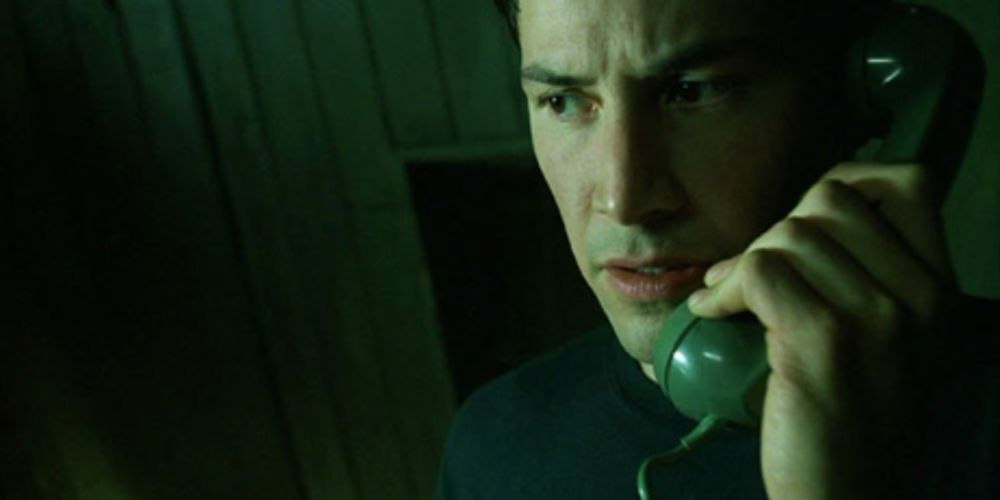 Neo (Keanu Reeves) picks up his green phone and speaks with Morpheus. 