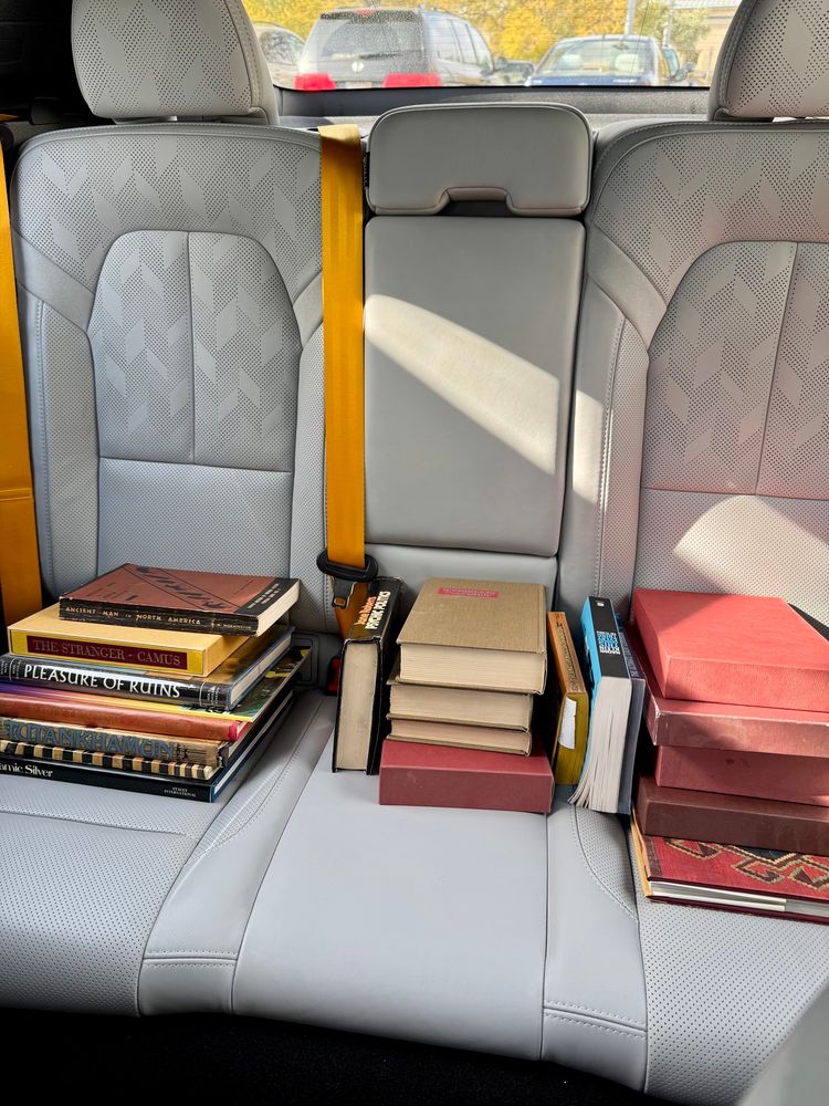 Three short stacks of older hardcover books in the backseat of a car.