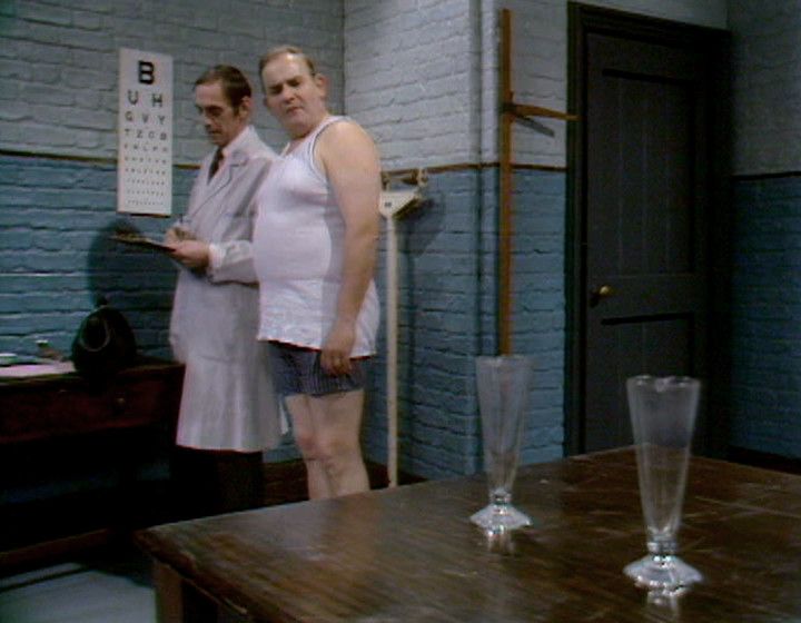 Fletcher looking questioningly at a couple of flasks in Porridge