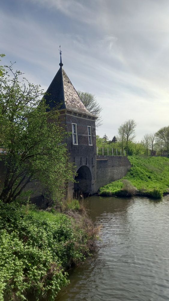 A 16th-century brick watergate rises over a moat with a green bank