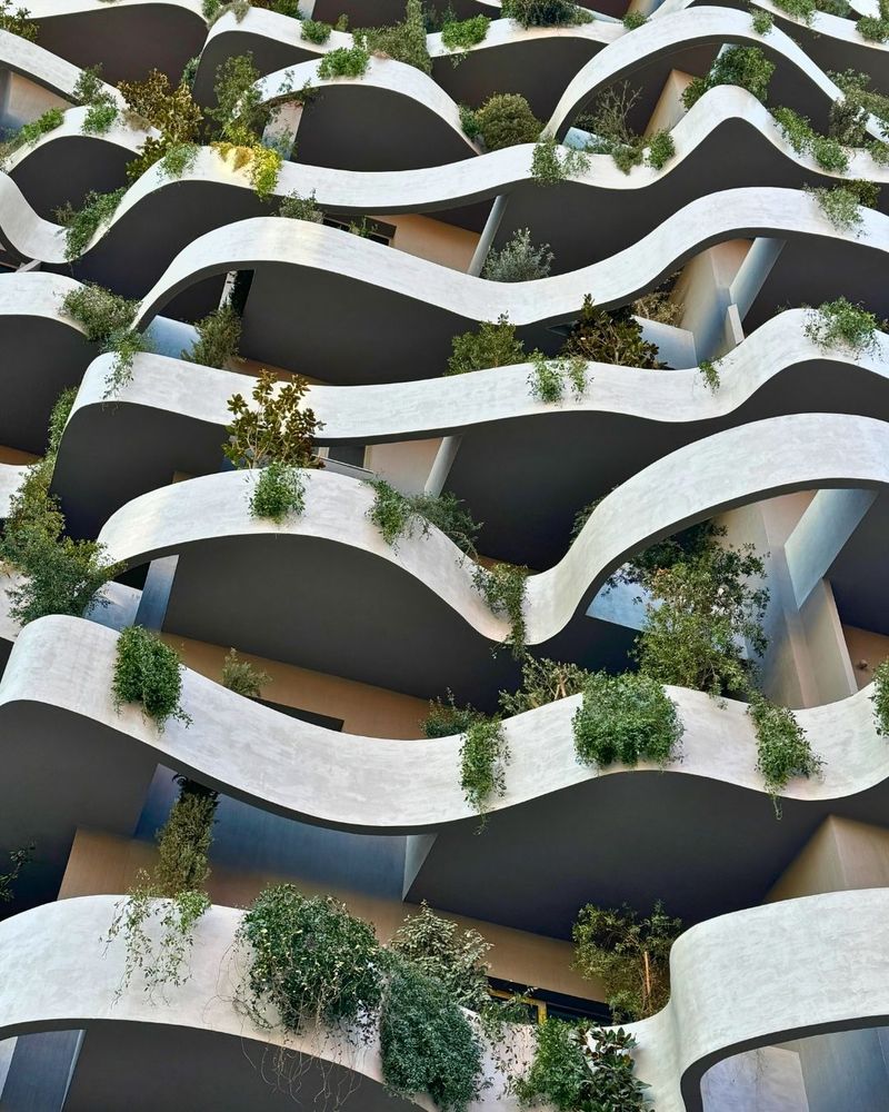 Photo showing the curved lines of a new building. Each level has plants and vines hanging over the ledge.