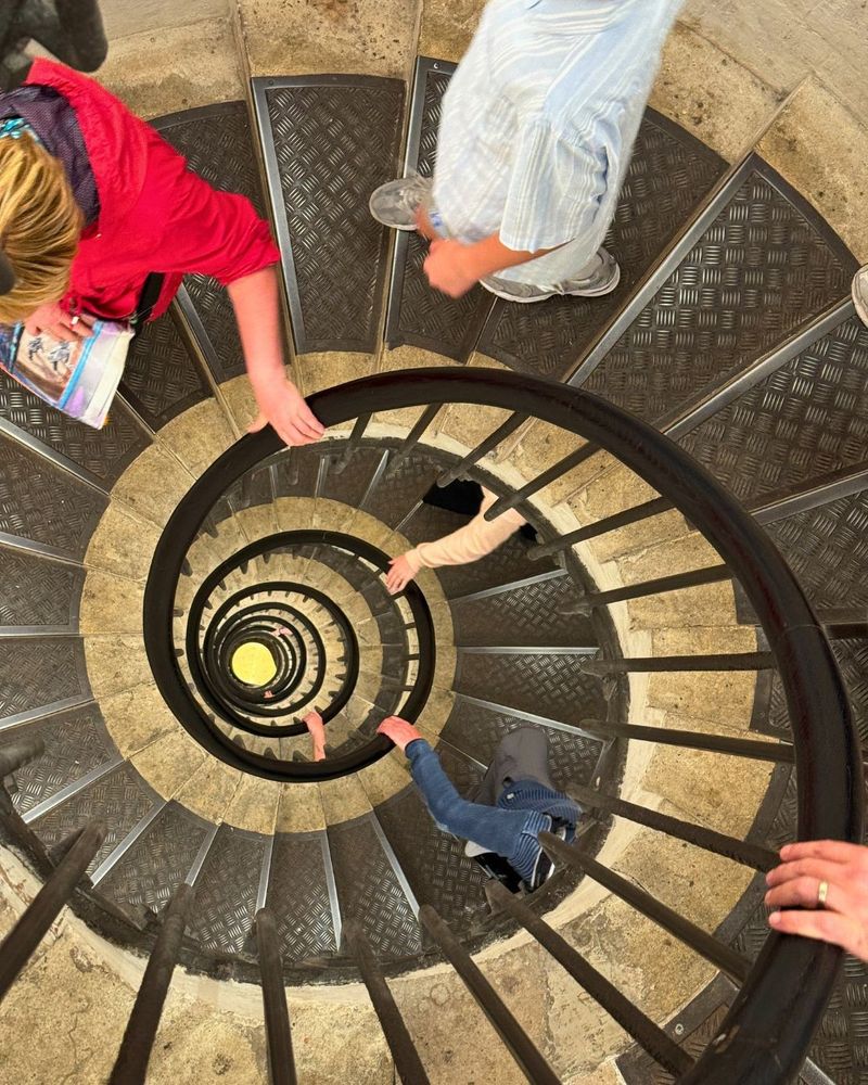 Photo looking down the center of a long spiral staircase inside the Arc de Triomphe in Paris France.